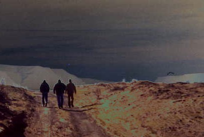 3 men walking down a road to nowhere. Over them glides a blue orb. To their right cavorts an aero-snake creature